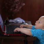 Boy Wearing Blue T Shirt Using Black Laptop Computer in a Dim Lighted Scenario